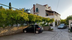 Een woonstraat met twee geparkeerde auto's, een stenen muur en een gebouw met een balkon en een rondboogvormige ingang.