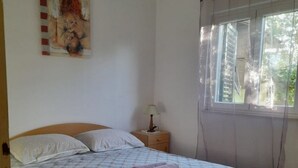 Een slaapkamer met een houten bed, een nachtkastje met een lamp, een raam met gordijnen en een schilderij aan de muur.
