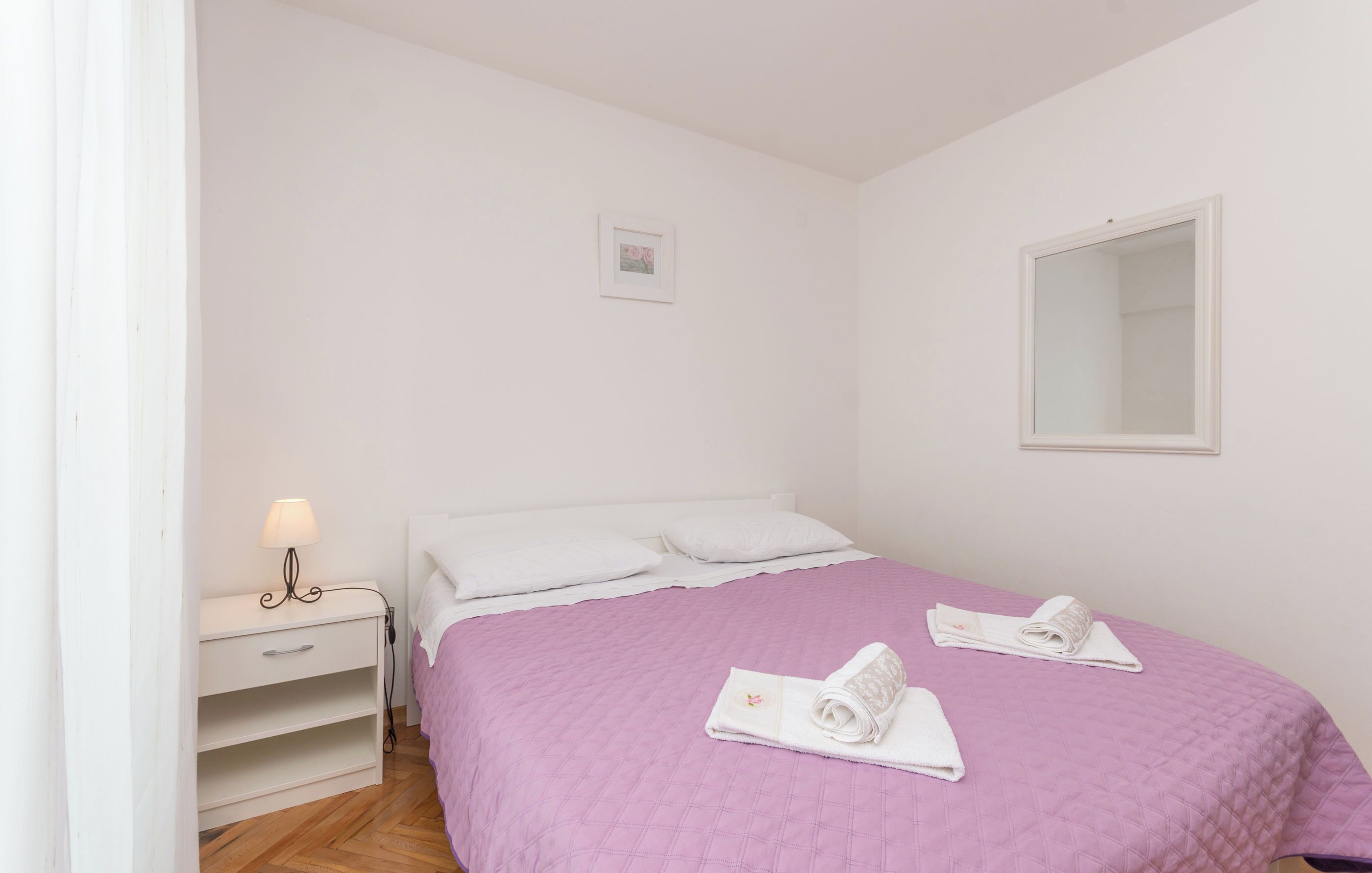 A neatly made bed with a pink quilt, a bedside table with a lamp, and two towels on the bed.