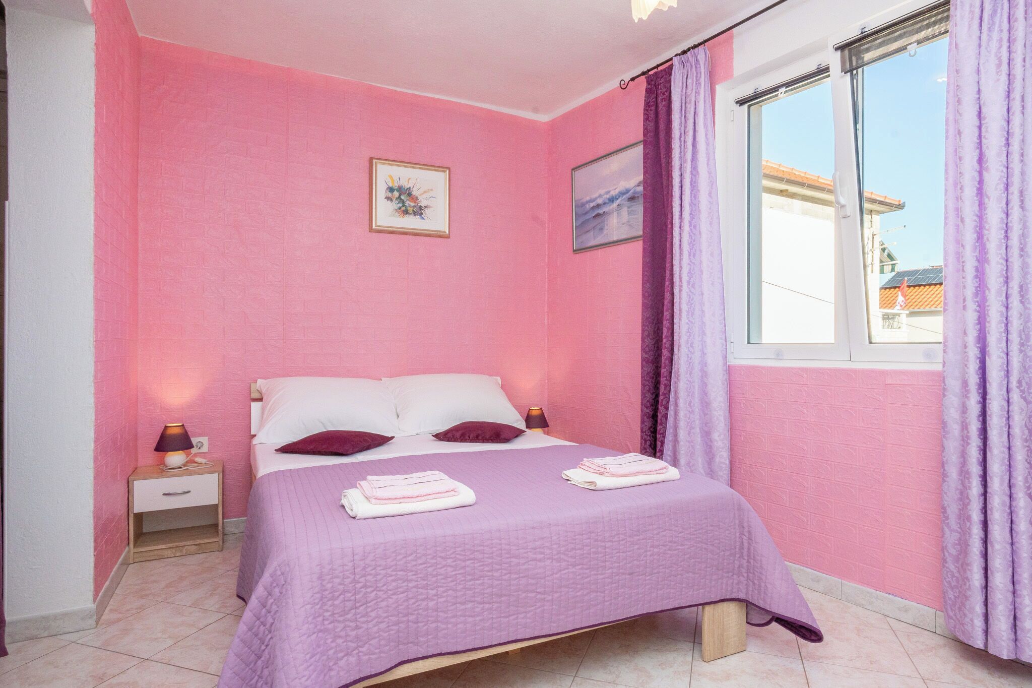 A bedroom with a bed, a nightstand, a lamp, and a window with curtains.