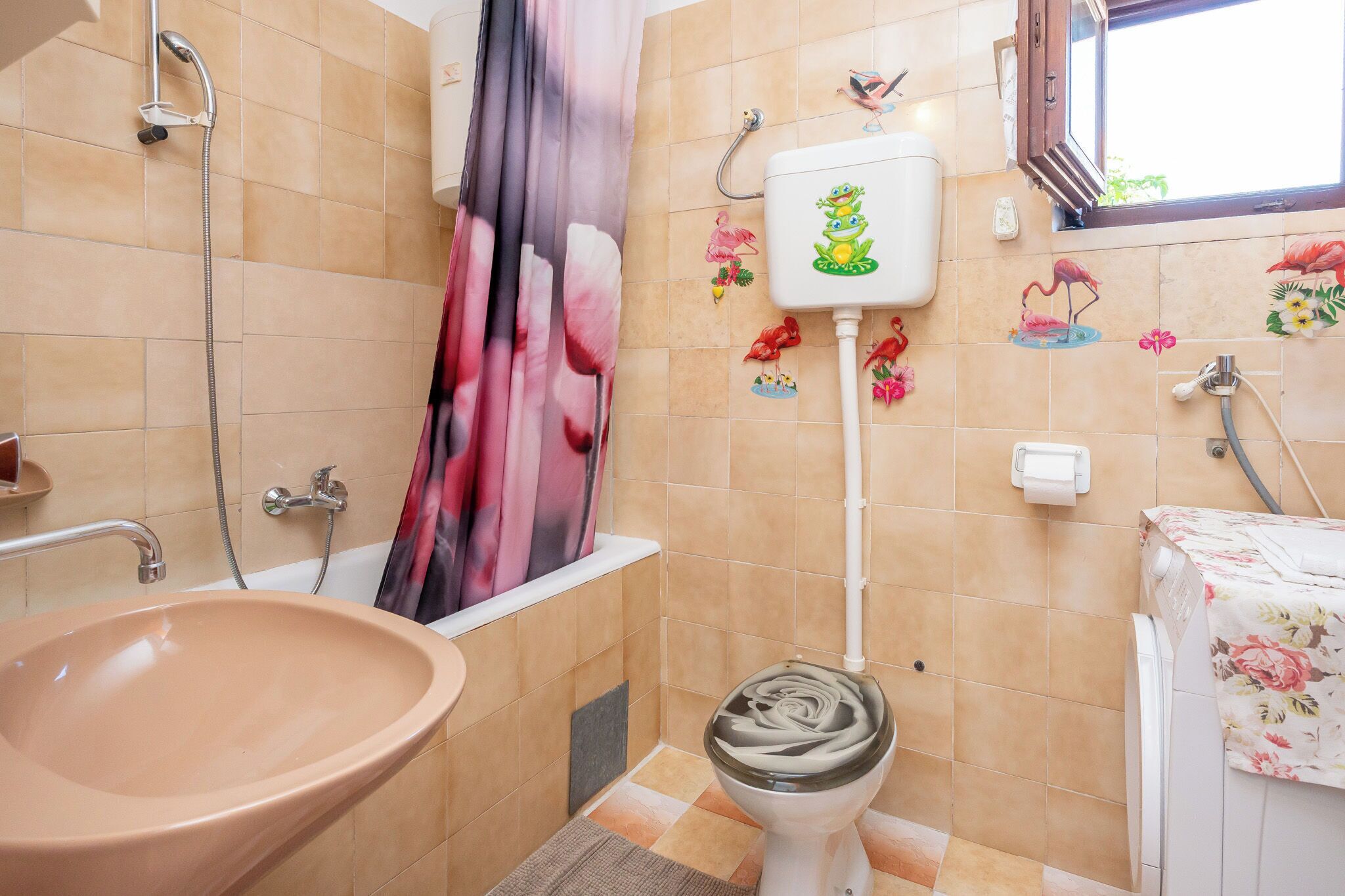 Un baño con un lavabo color beige, un inodoro, una ducha y una ventana.
