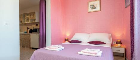Un dormitorio con una cama, almohadas, una mesita de noche, una lámpara y un baño a la vista al fondo.