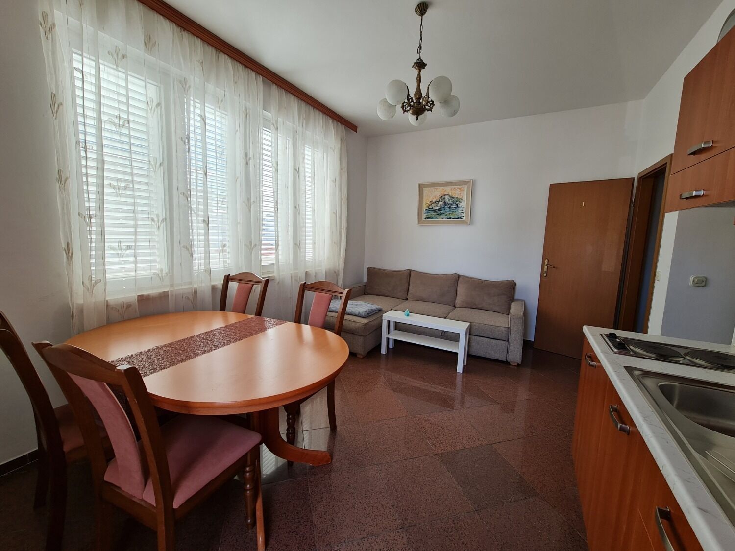 Un coin repas avec une table ronde et des chaises, un canapé, une petite table basse blanche et un espace cuisine comprenant un évier et des placards.