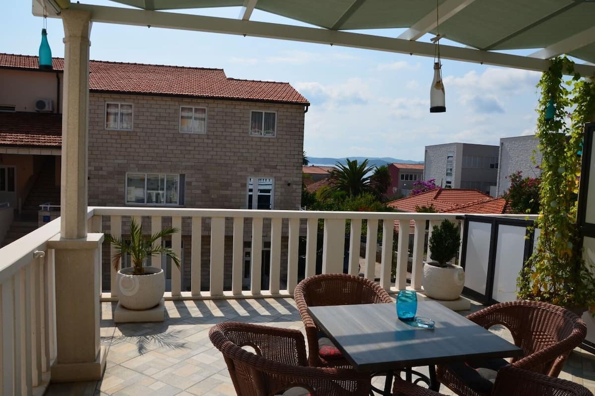 A balcony with wicker furniture and potted plants, overlooking a building with a tiled roof.