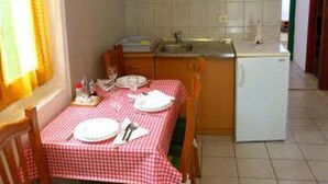 A compact kitchen with wooden cabinets, a white refrigerator, and a dining table set with plates and cutlery. - House Kuca za Odmor (Preko)