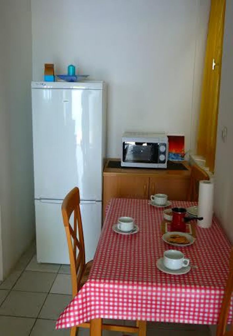 A compact kitchen with a refrigerator, microwave, and a table set with cups and a teapot.