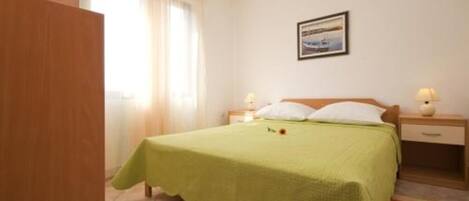 A hotel room with a bed, a nightstand, a lamp, a window with curtains, and a painting on the wall.