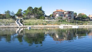 A waterfront property with a stone staircase leading to a dock, surrounded by trees and buildings with red roofs. - Apartments Ljilja (Nin)