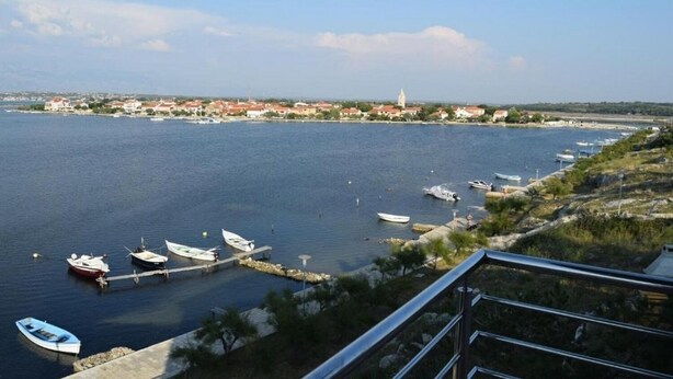 A coastal marina with boats docked, a clear sky, and a distant town with buildings. - Apartments Ljilja (Nin)