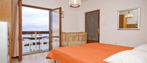 A bedroom with a bed, a crib, a view of the sea, and a dining area with a table and chairs.