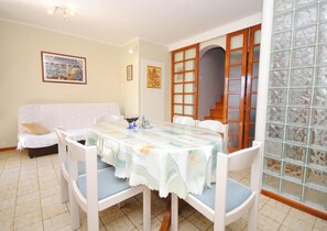 A dining area with a table set for four, surrounded by white chairs. A white sofa is against the wall, and there are framed pictures on the wall. - Apartment Rina (Okrug)