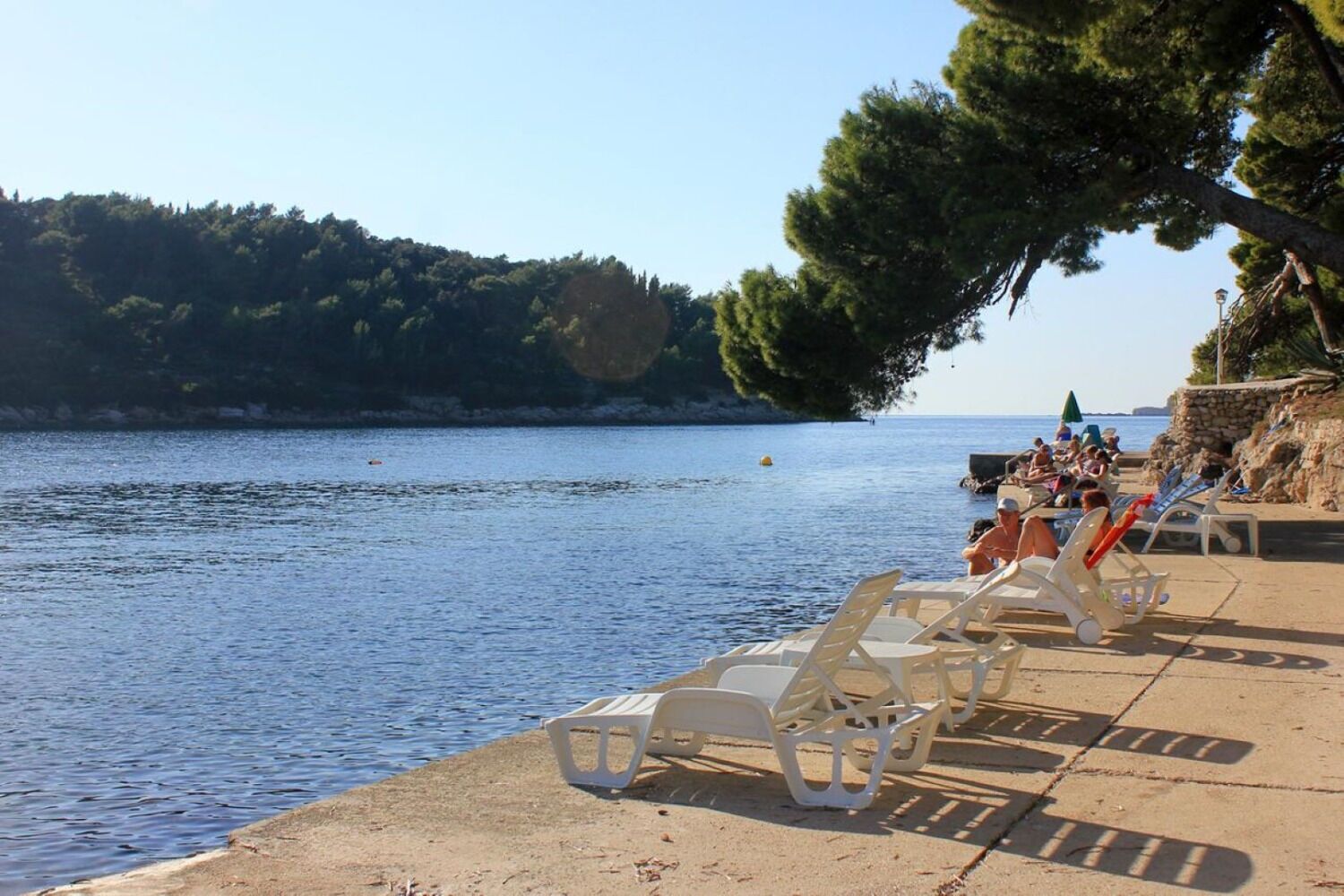 Un espace aménagé au bord de la plage, avec des chaises longues en plastique blanc et un mur en pierre.