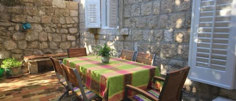 A stone-walled patio with a table set for four, surrounded by wooden chairs.