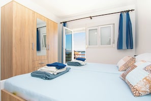 A bedroom with a bed, a wardrobe, a window with curtains, and a view of the outside.