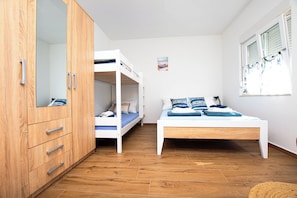 Une chambre avec un lit superposé, un lit simple, un plancher en bois et une armoire.