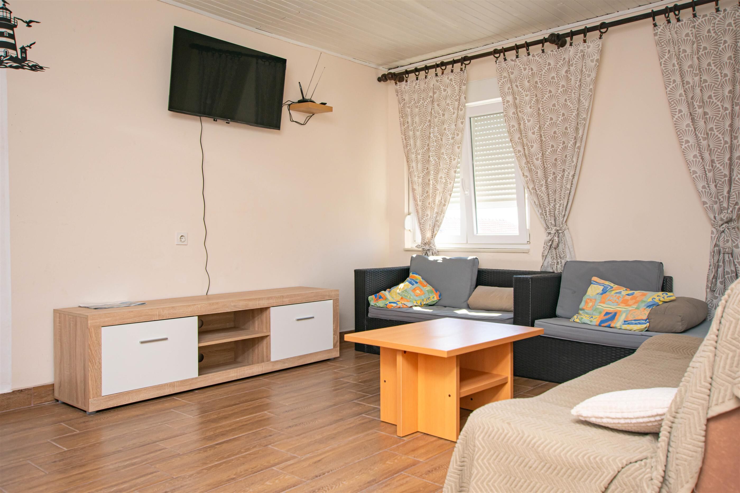 A living room with a sofa, a wooden TV stand, a small table, and a window with curtains.
