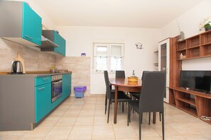 Une cuisine avec des meubles de couleur turquoise, une table à manger avec des chaises, un meuble pour la télévision et une poubelle.