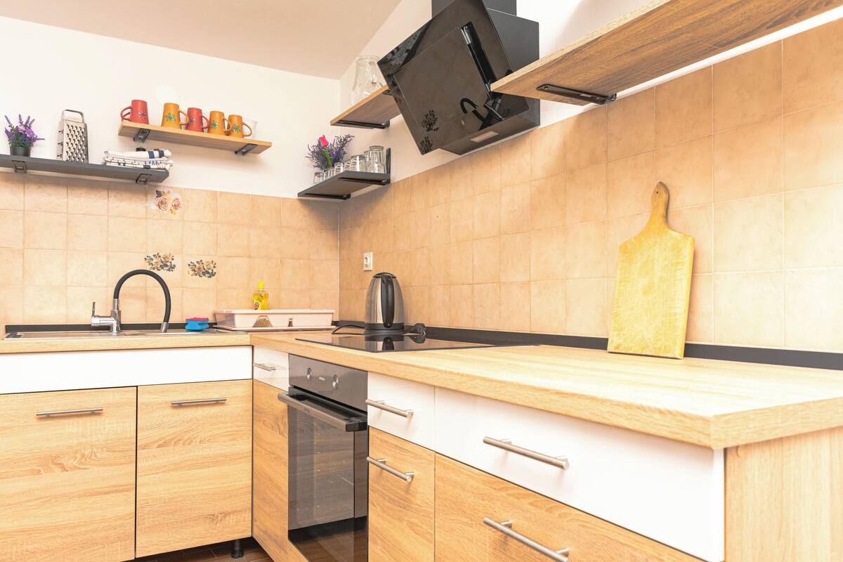 A kitchen with wooden cabinets, a stainless steel sink, a built-in oven, and a wooden cutting board.