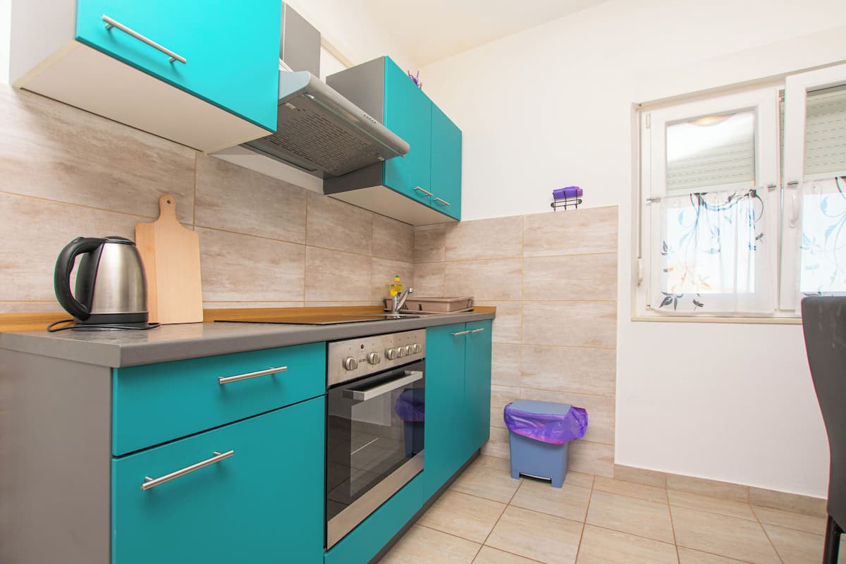 A kitchen with teal cabinets, a stainless steel oven, a sink, and a window with curtains.