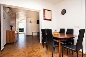 A dining area with a wooden table and black chairs, a clock on the wall, and a brick wall.