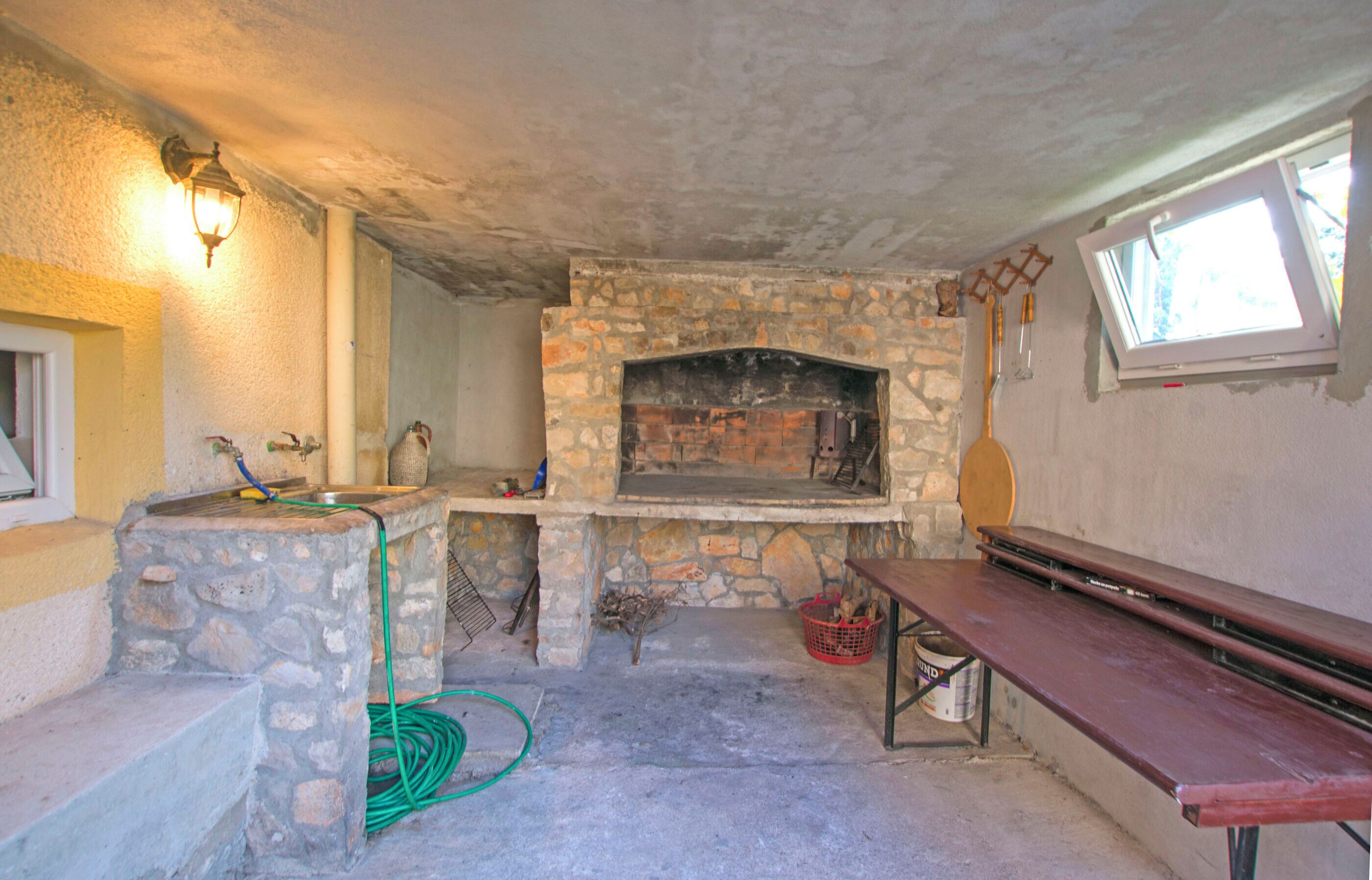 Ein Steinkamin mit Fenster darüber, eine Bank und ein Schlauch auf dem Boden.