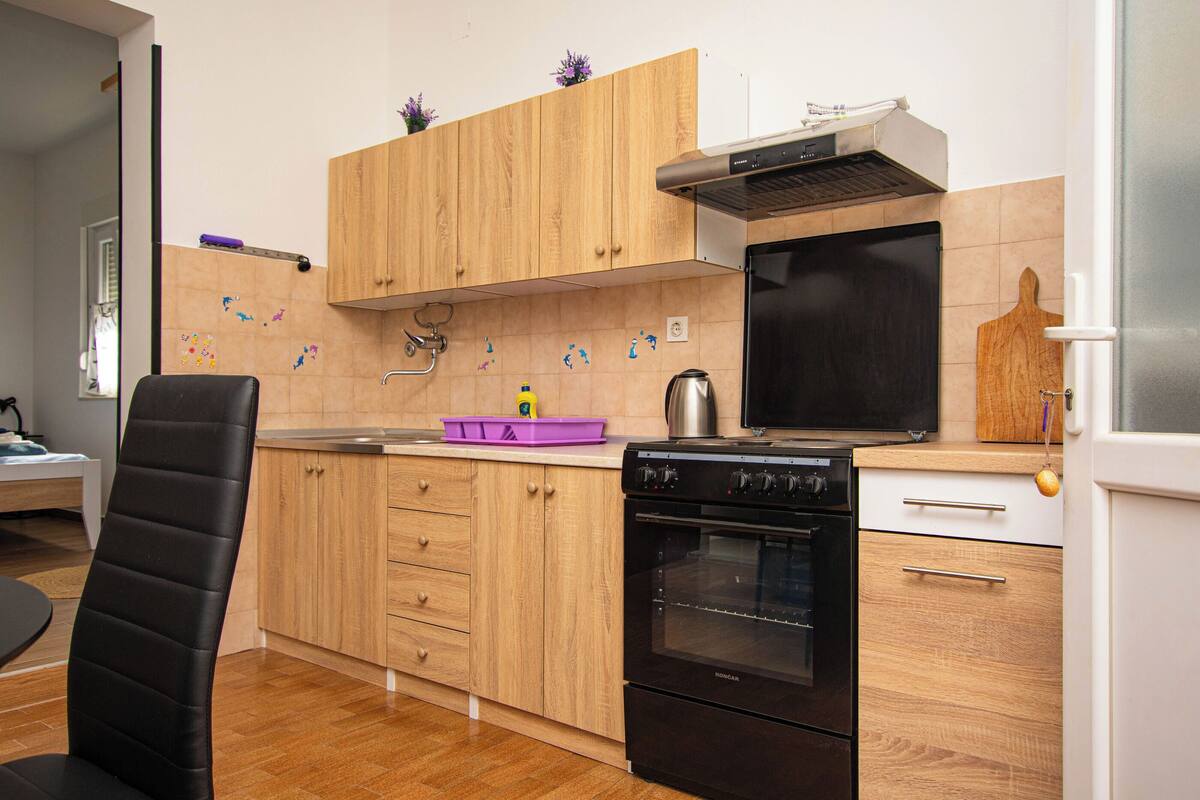 A kitchen with wooden cabinets, a black oven, a sink, and a chair.