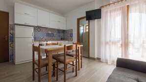 A compact kitchen with white cabinets, a tiled backsplash, and a dining area with a table and chairs. - Apartments Armitage (Privlaka)