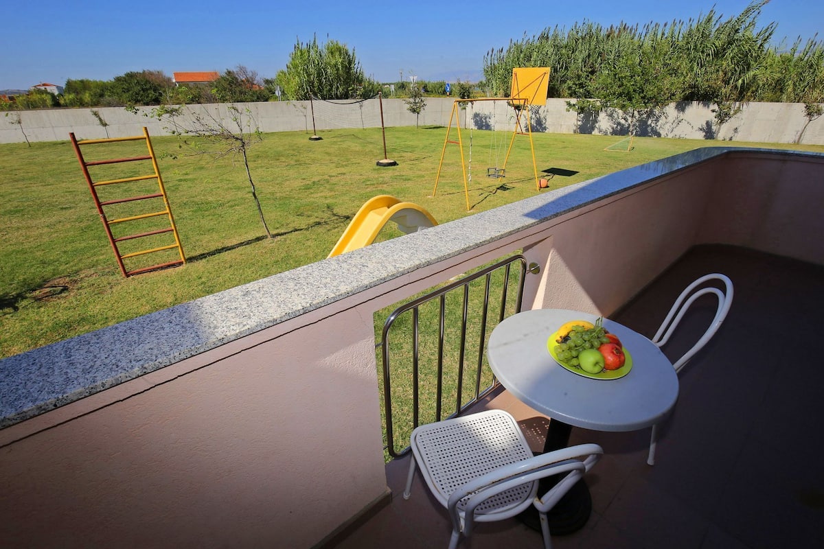 Un balcón con mesa y sillas, un pequeño jardín con un columpio y vistas a una zona residencial.