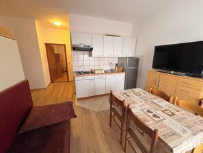 A compact kitchen with white cabinets, a gas stove, a refrigerator, and a television. - Apartments Armitage (Privlaka)