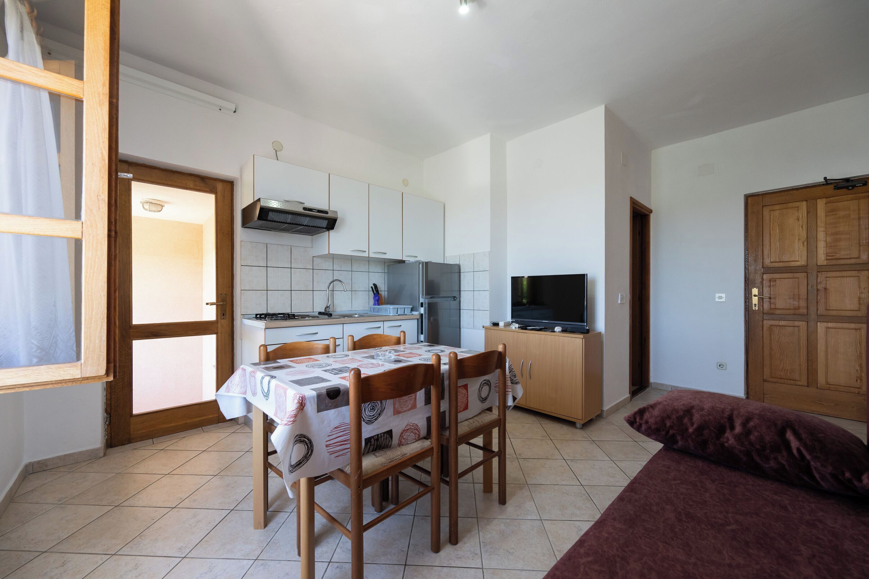 A compact kitchen with a dining table, chairs, a TV, and a sofa.