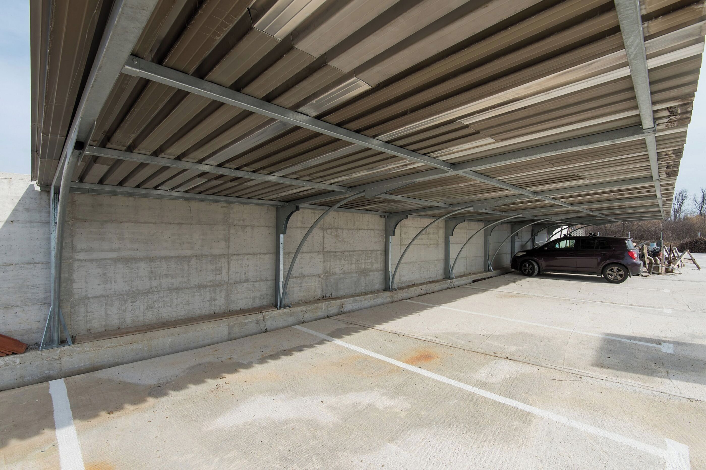 A covered parking area with concrete walls and a metal roof structure.