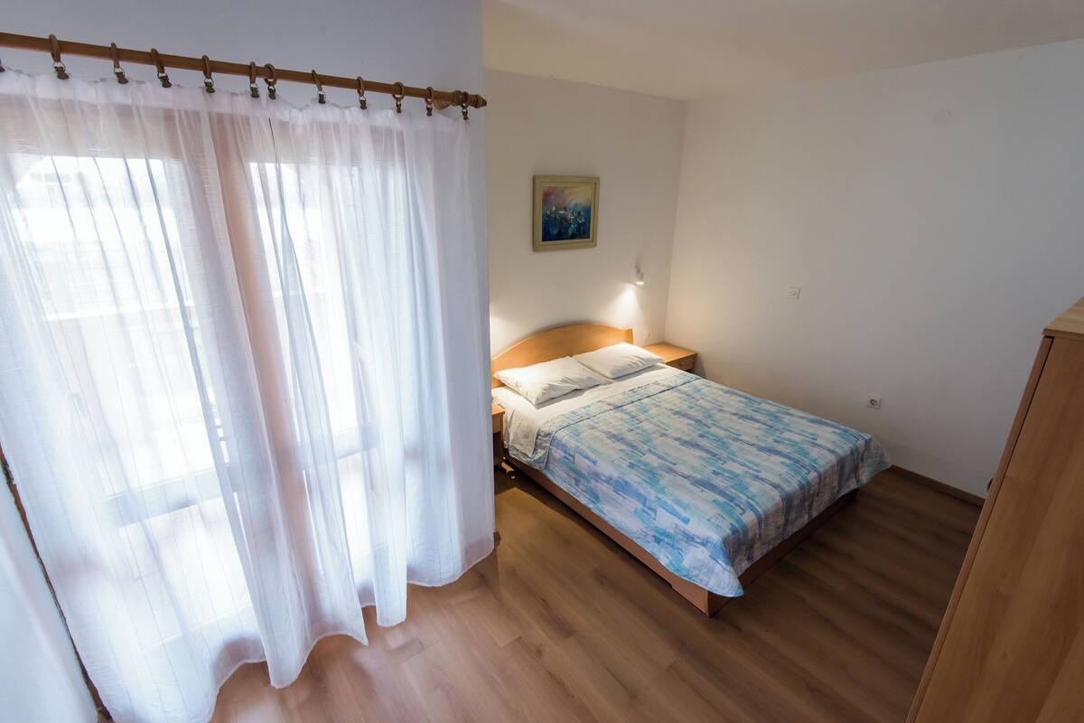 Ein Schlafzimmer mit einem Bett, Holzboden, einem Nachttisch, einer Lampe und einem Gemälde an der Wand.