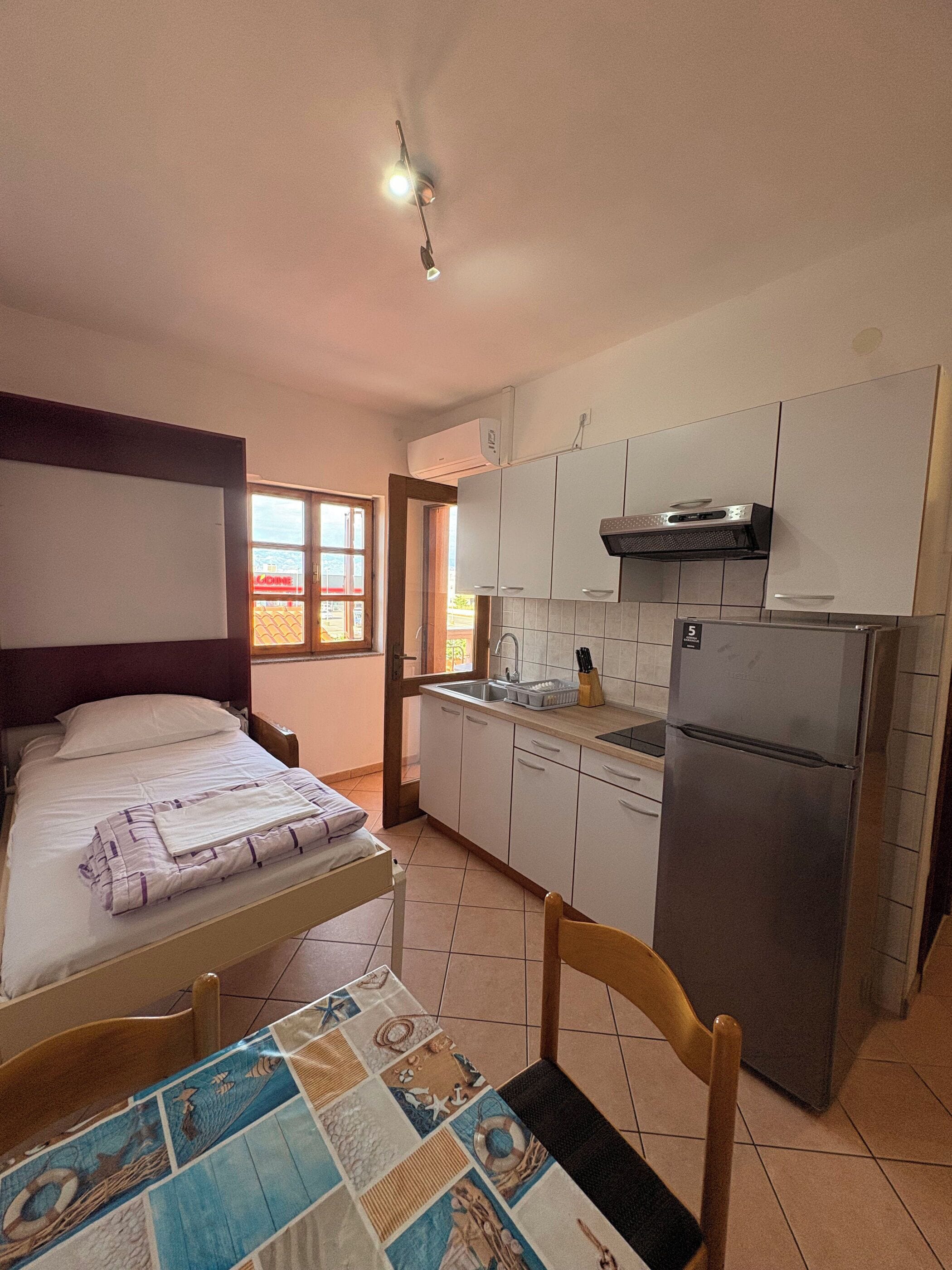 A compact kitchen with a bed, a dining table with a placemat, and a refrigerator.