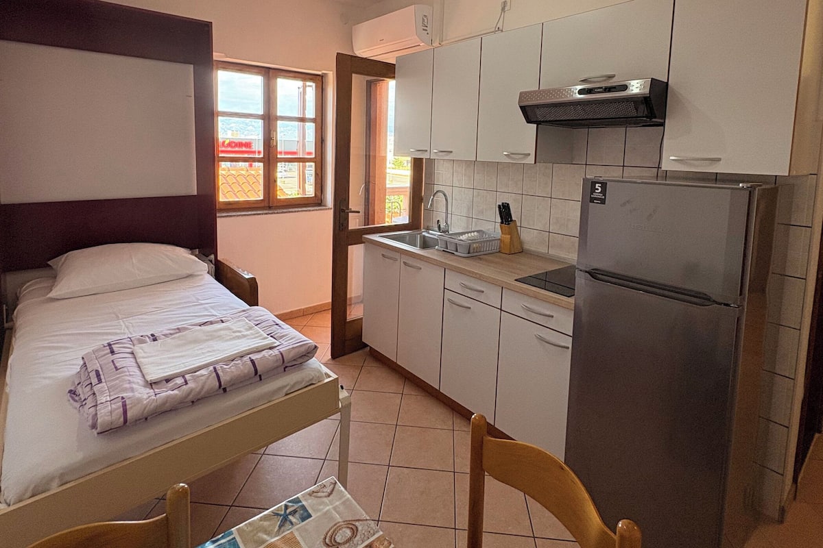 Una cocina compacta con cama, una mesa de comedor con un mantel individual y un refrigerador.