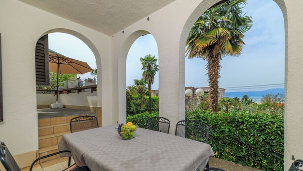 A covered outdoor dining area with a table and chairs, a fruit bowl, and a view of the sea. - Apartment Renata (Omisalj)