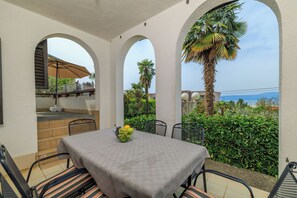 A covered outdoor dining area with a table and chairs, a fruit bowl, and a view of the sea. - Apartment Renata (Omisalj)