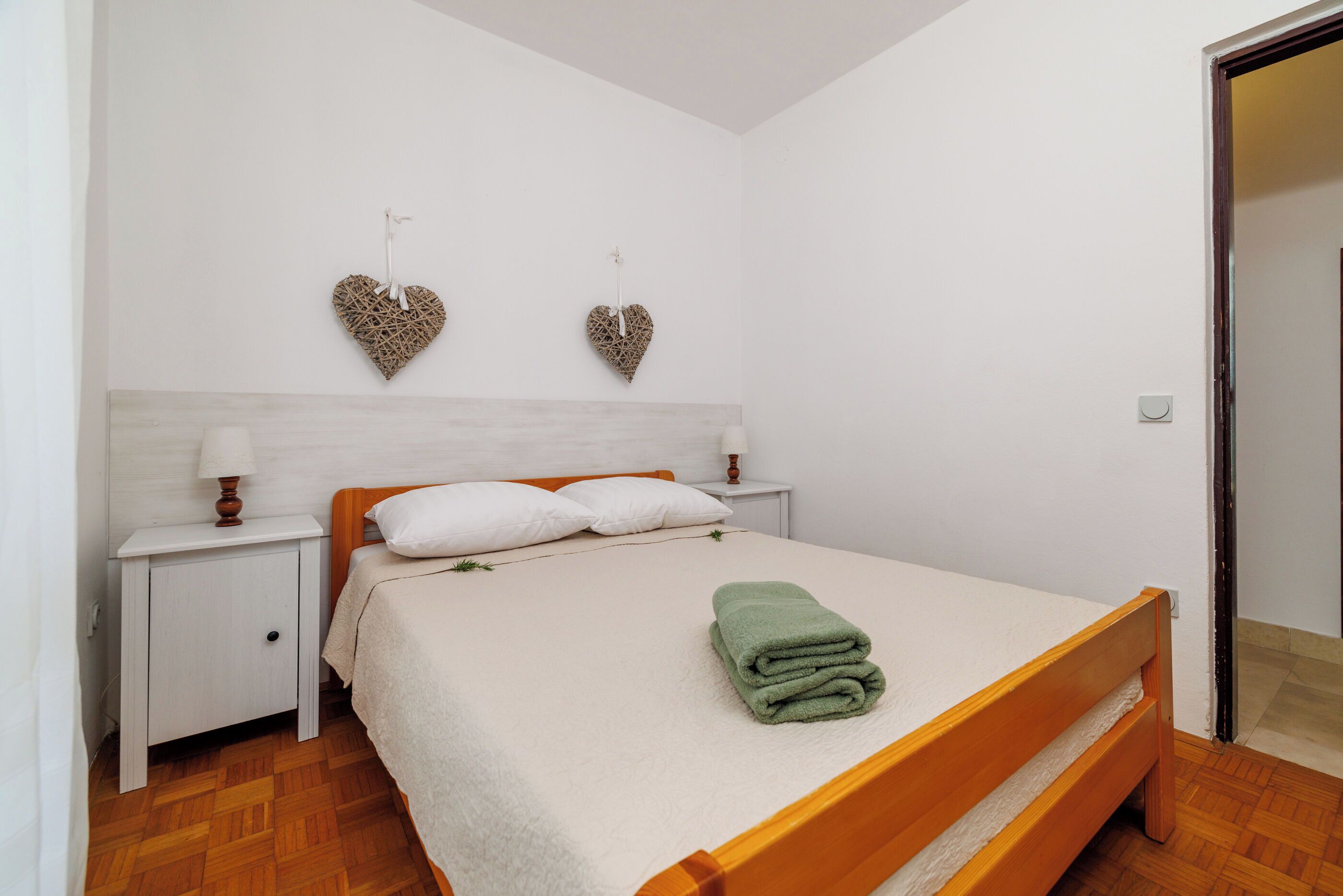 A bedroom with a bed, nightstands, and decorative heart wall hangings.
