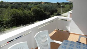 Een balkon met een tafel en stoelen, met uitzicht op een landschap met struiken en een gebouw in de verte.
