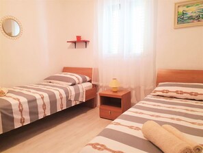 A room with two single beds, a small table with a lamp, a shelf with a red object, and a painting on the wall. - Apartment Roko (Vis)