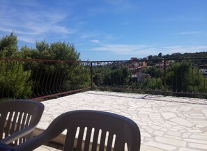 Eine Terrasse mit Steinplatten, Metallgeländer und zwei Plastikstühlen.