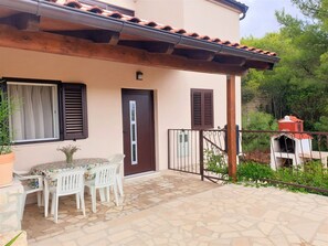 A patio with a table and chairs, a door, and a small outdoor grill. - Apartment Roko (Vis)