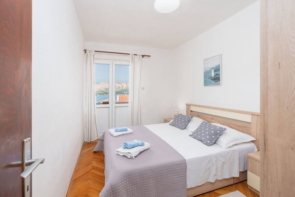 Une chambre à coucher avec un lit, une table de chevet, une fenêtre avec des rideaux et une vue sur l’extérieur.