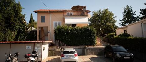A residential building with a tiled roof, a staircase leading to a balcony, and a paved driveway.