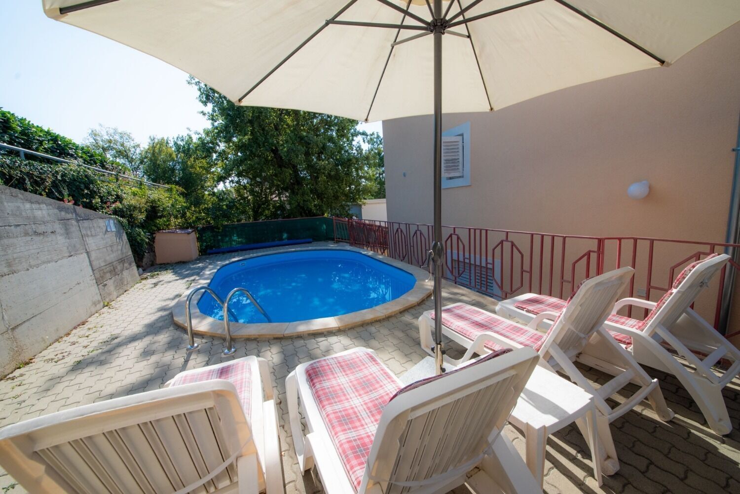 Una piscina exterior amb gandules i un parasol gran.