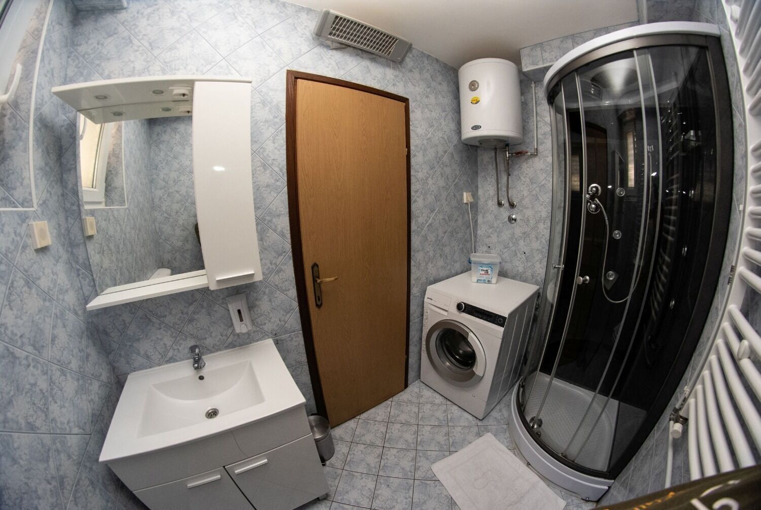 Et moderne badeværelse med vask, spejl, toilet, brusebad og vaskemaskine.