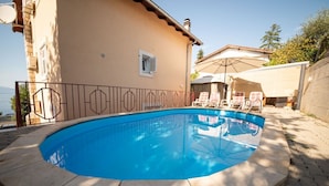 A swimming pool with a geometric tile design, surrounded by a concrete deck and a metal fence. - Apartment Ivona (Omisalj)