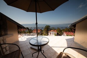 A terrace with a round table and chairs, an umbrella, and a view of the sea and houses in the background. - Apartment Ivona (Omisalj)