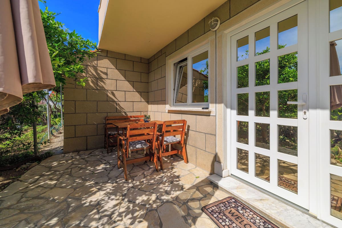 A patio with a stone floor, wooden table and chairs, a window, and a door.
