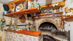 A stone fireplace with a wooden shelf above it, filled with various bottles and kitchen items. - Apartments Tatjana (Rab)