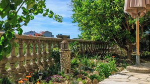 A garden with a stone pathway, a stone fence, and a variety of plants and flowers. - Apartments Tatjana (Rab)